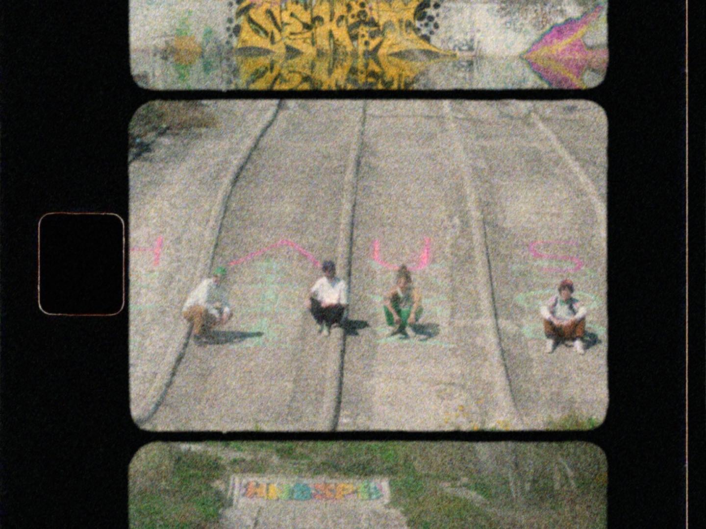 The four members of Hause Plants are sitted on the ground of and abandoned water park. There's graffitis everywhere.